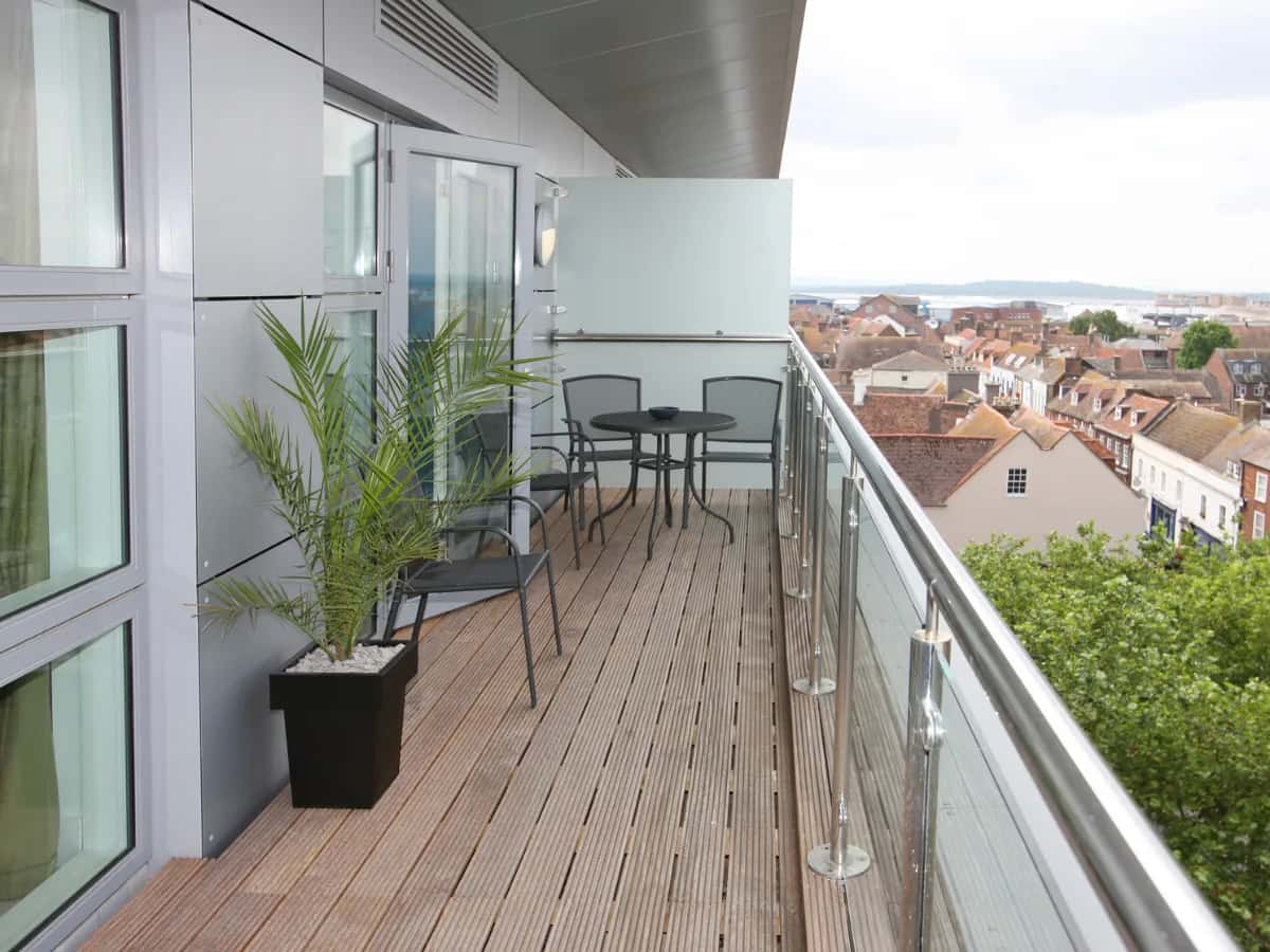 Balcon en lames de bois avec table et chaises, au-dessus des toits d'une ville