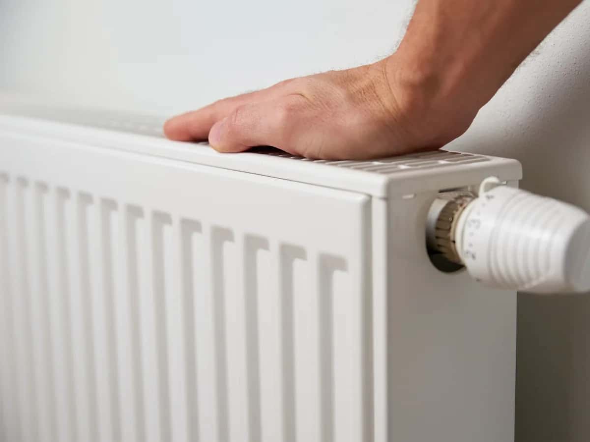 Main posée sur un radiateur à eau équipé d'un robinet thermostatique